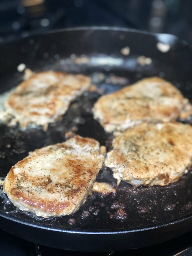pork chops cooking in a cast iron pan