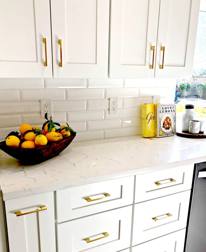 white kitchen cupboards with gold hardware and a bowl of lemons on the countertop