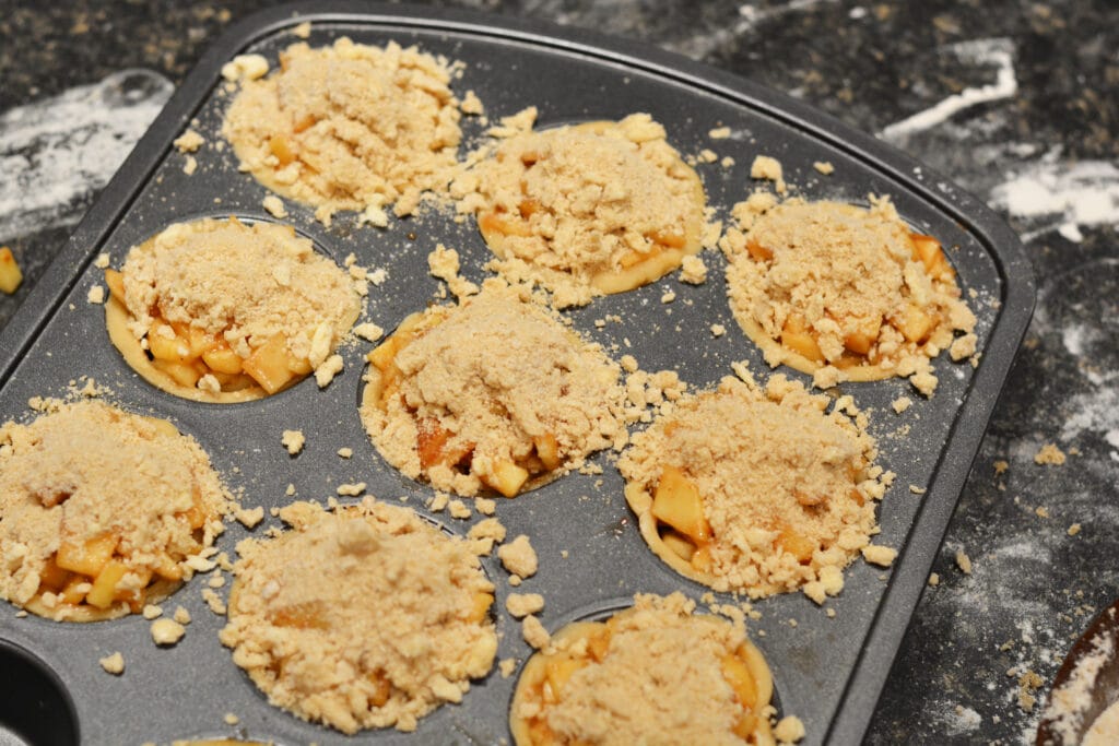 sprinkling topping on mini apple pies