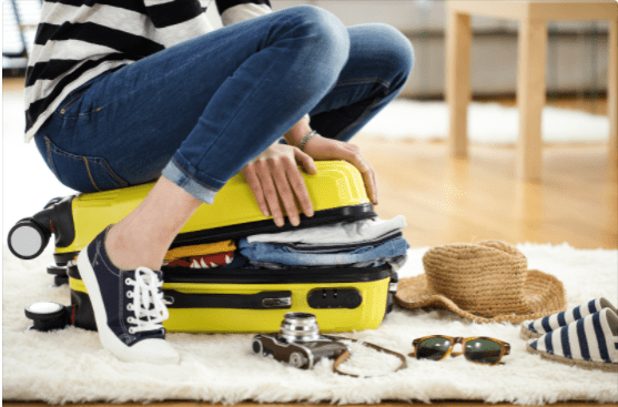 woman sitting on a suitcase trying to close it