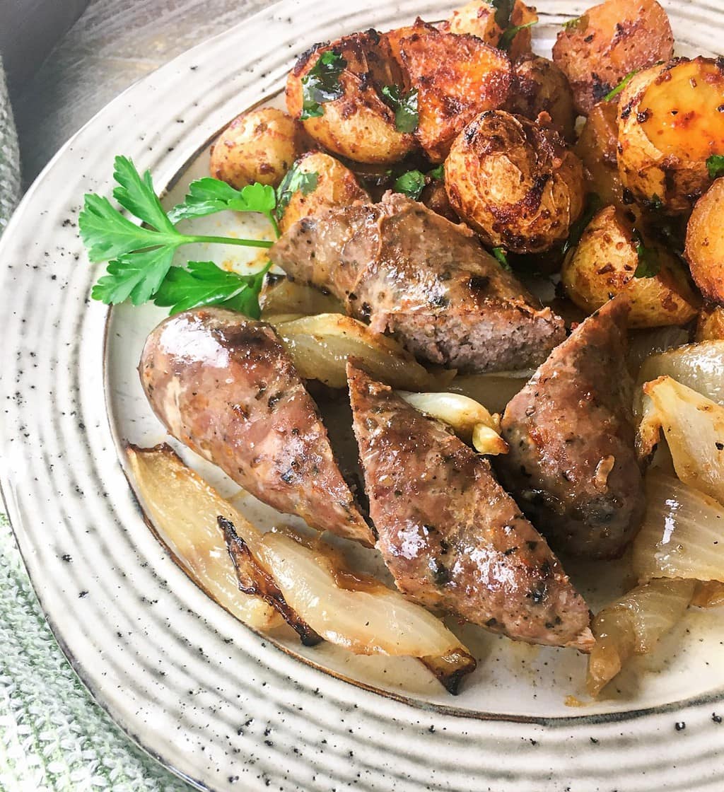 chorizo with spanish-style potatoes and a sprig of parsley on a white plate