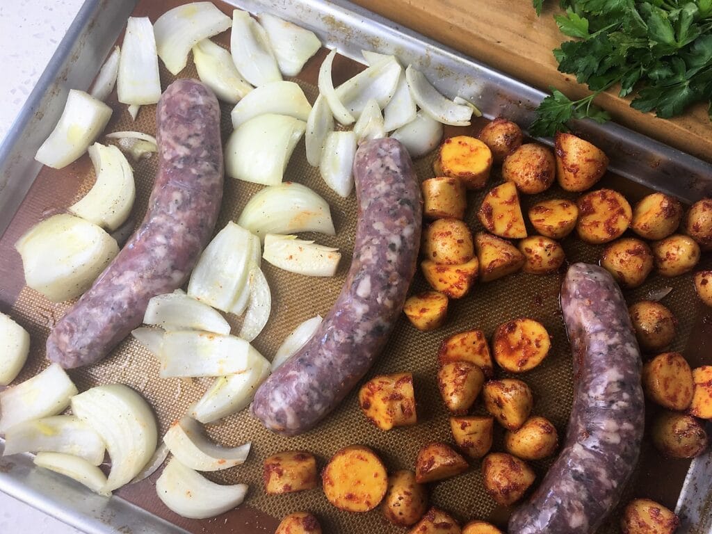 chopped onions, paprika sprinkled potatoes and uncooled chorizo on a sheet pan