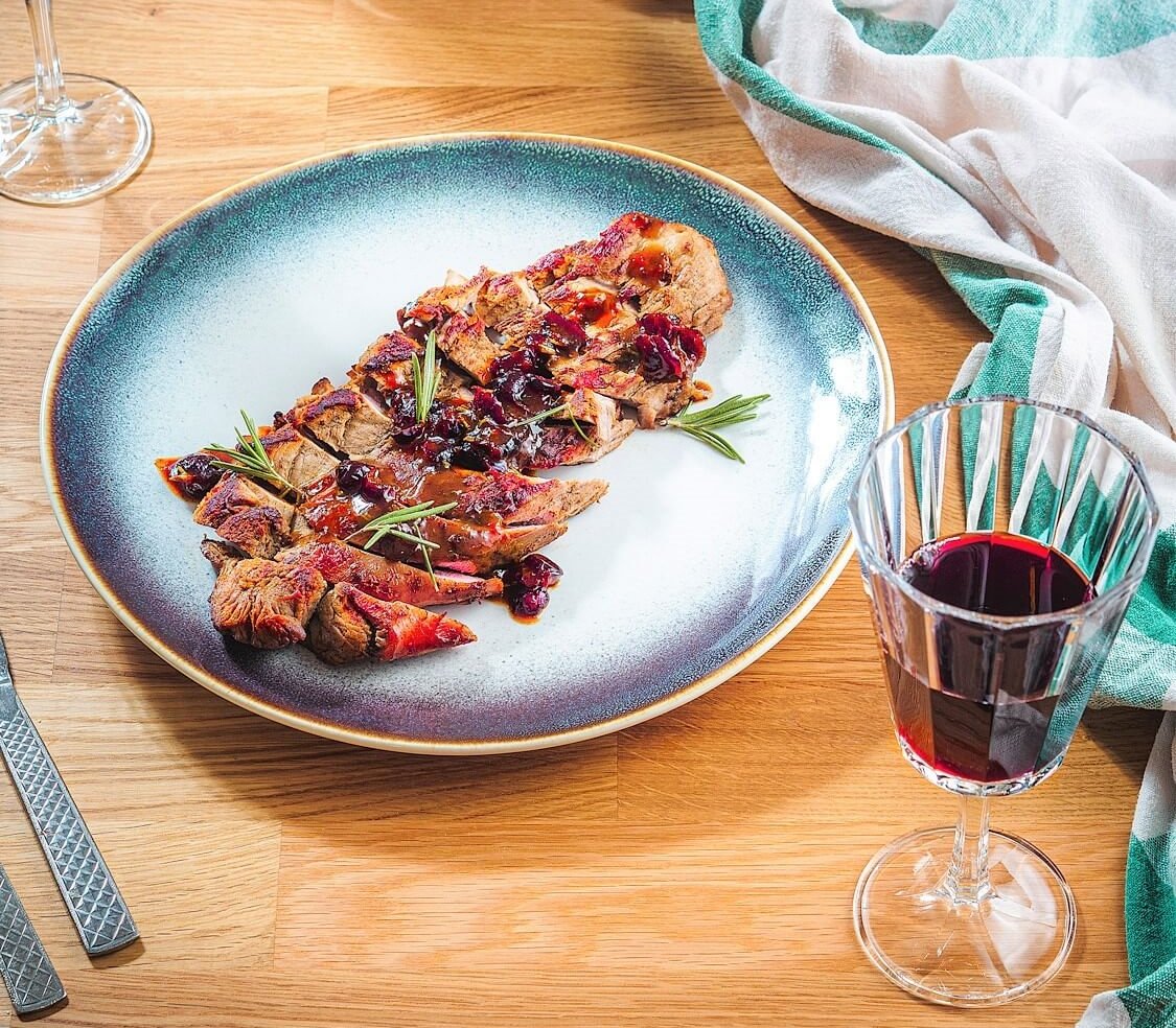 Red wine beside a CranberryOrangePork Tenderloin on a plate