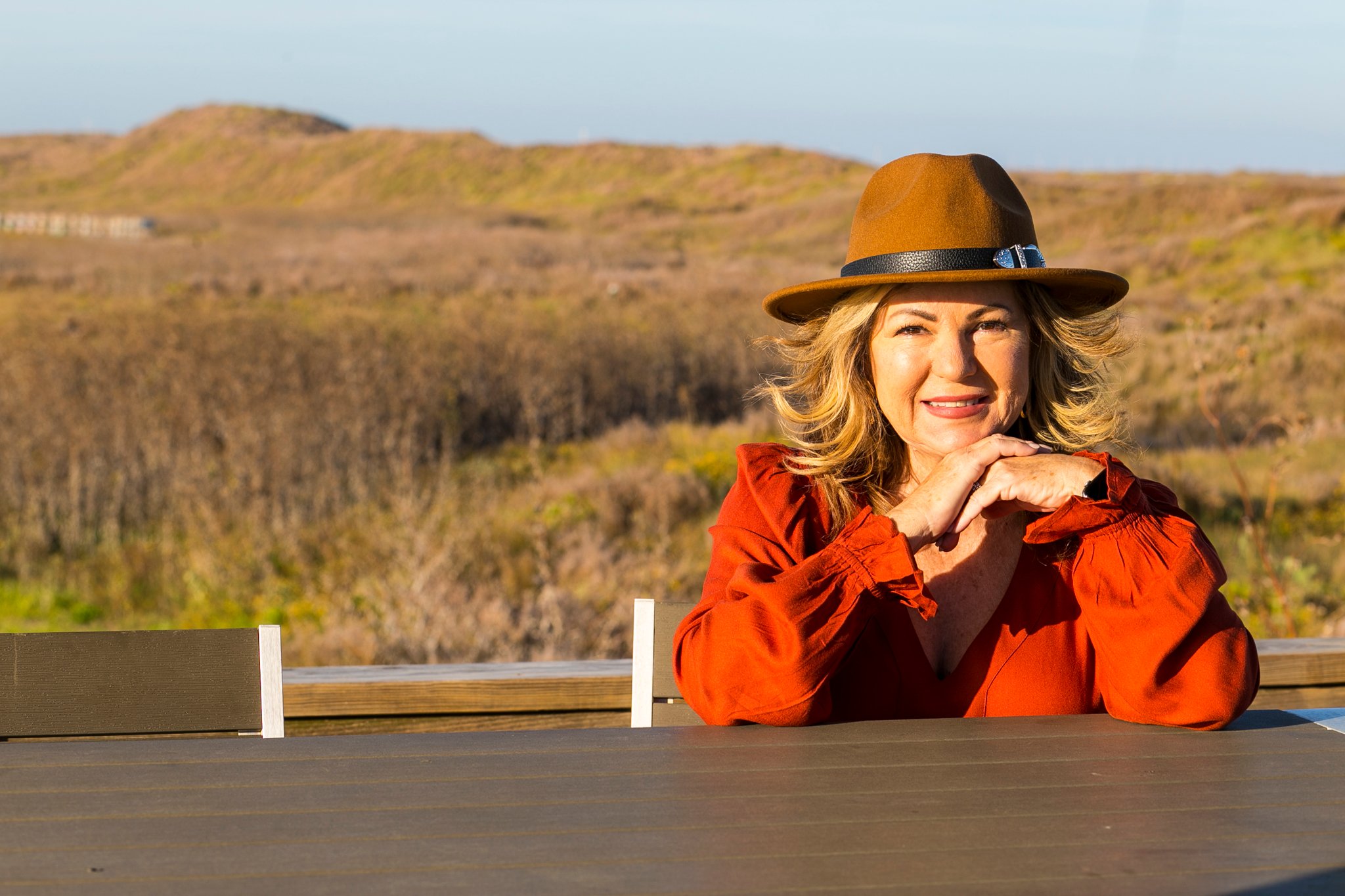 Lori Felix wearing a brown felt hat posing with hands clasped