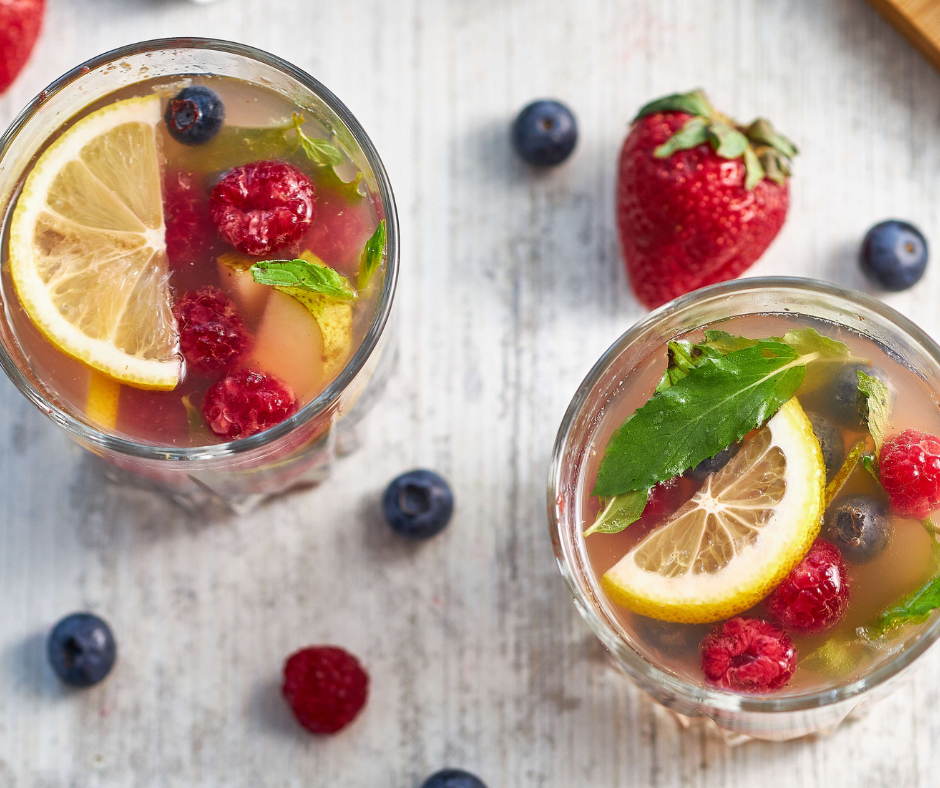 two glasses of nerry sangria garnished with sliced lemons and mint leaves
