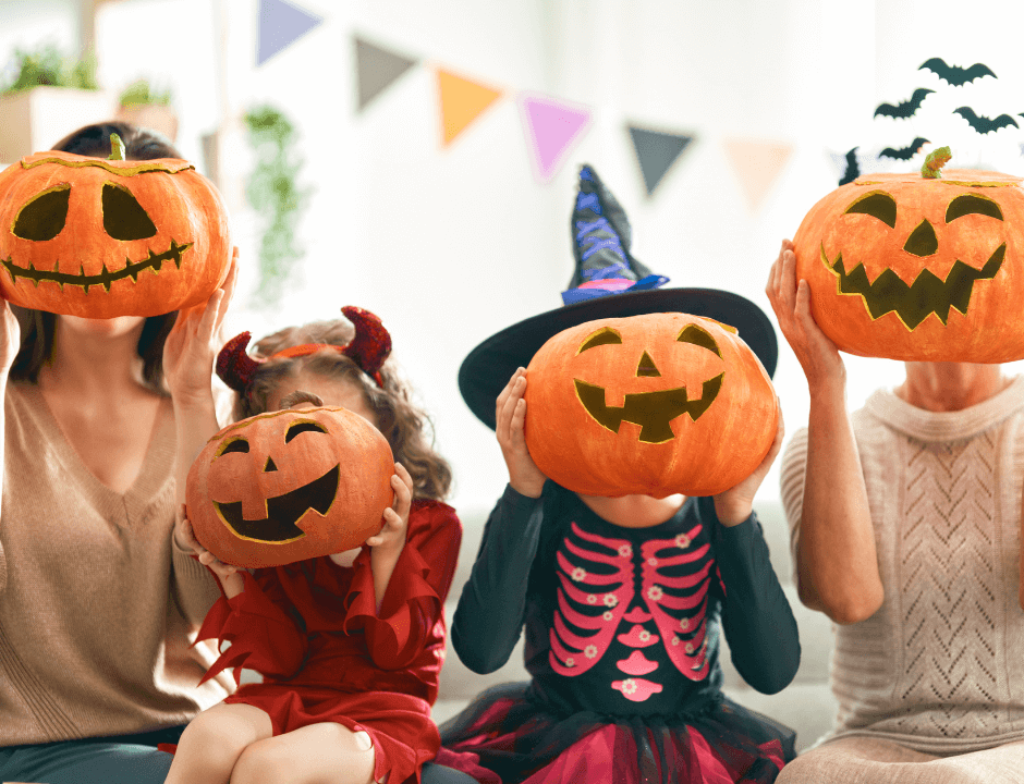 Two adults and two kids in costumes holding up carved pumpkins