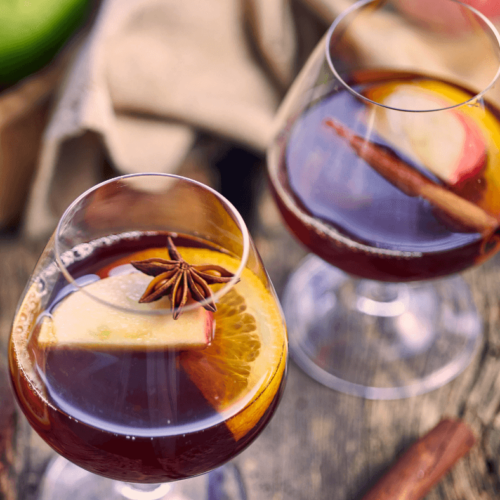 Two glasses of Spiked Hot Apple Punch garnished with orange and apple slices and cinnamon sticks