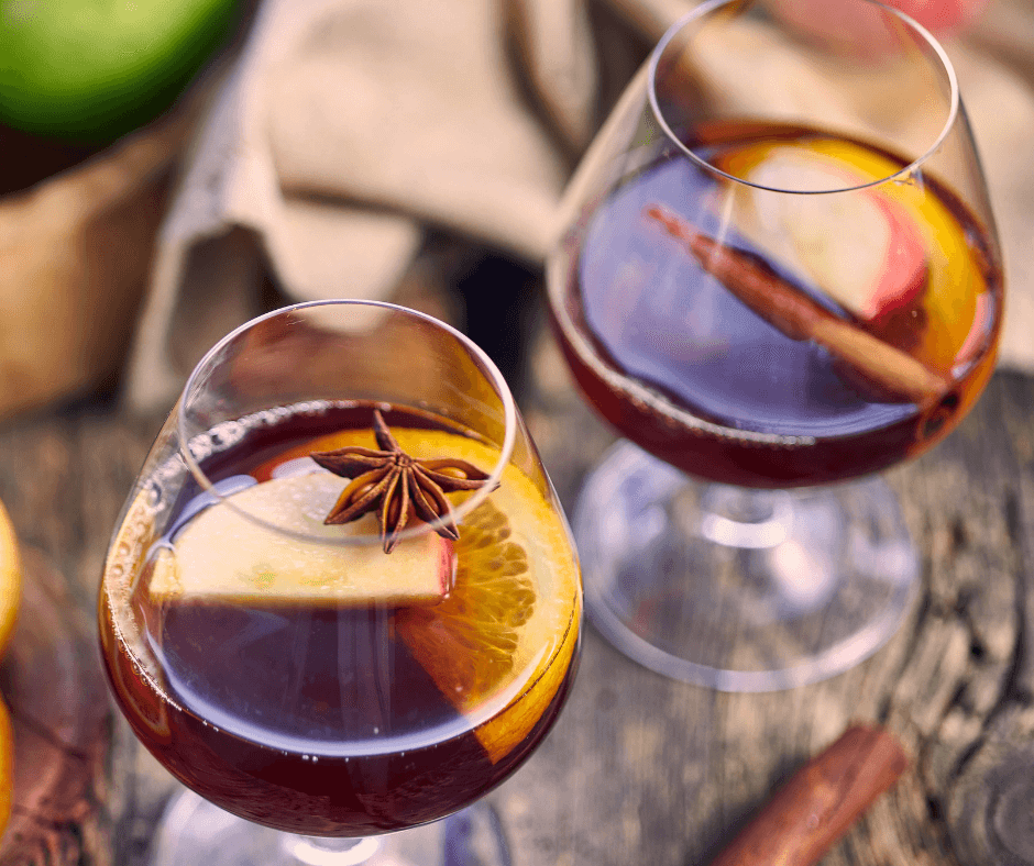 Two glasses of Spiked Hot Apple Punch garnished with orange and apple slices and cinnamon sticks