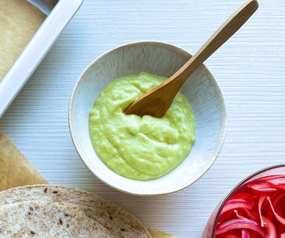 Creamy avocado sauce on a small bowl with a spoon for the Sweet Potato Tacos with Red Beans