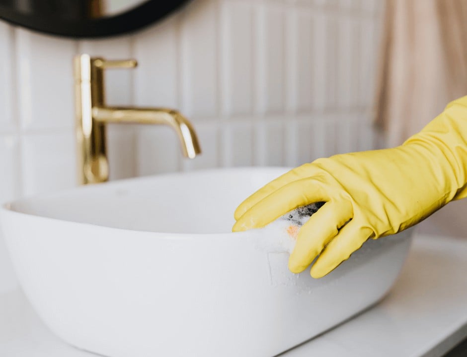 A person wearing gloves and cleaning the sink