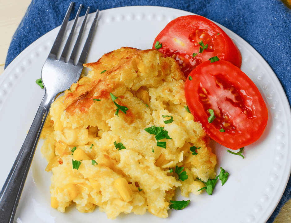 Easy Baked Corn Casserole served on a white plate with sliced tomatoes on the side