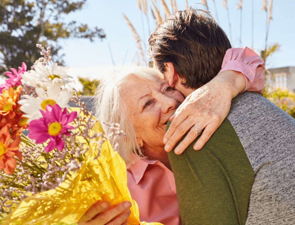 A man hugging his mother after giving her flowers