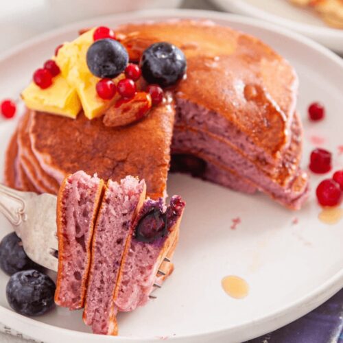 A serving of Spiced and Fluffy Purple Blueberry Pancakes on a white plate