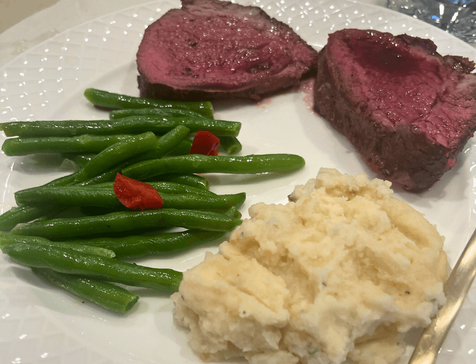 A plate of sliced Chateaubriand, a scoop of mashed potatoes, and green peas served on a white plate