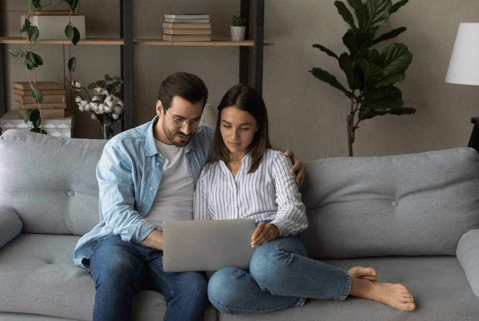 A couple sitting on the couch while looking at the laptop screen