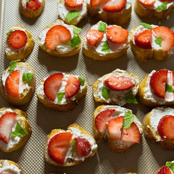 A closeup of sliced crostini with goat cheese, sliced strawberries, and mint